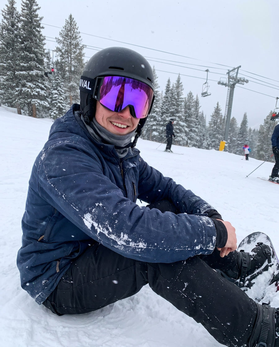 Snowboarder at the edge of a run wearing a NIVAL heated goggle with a purple lens